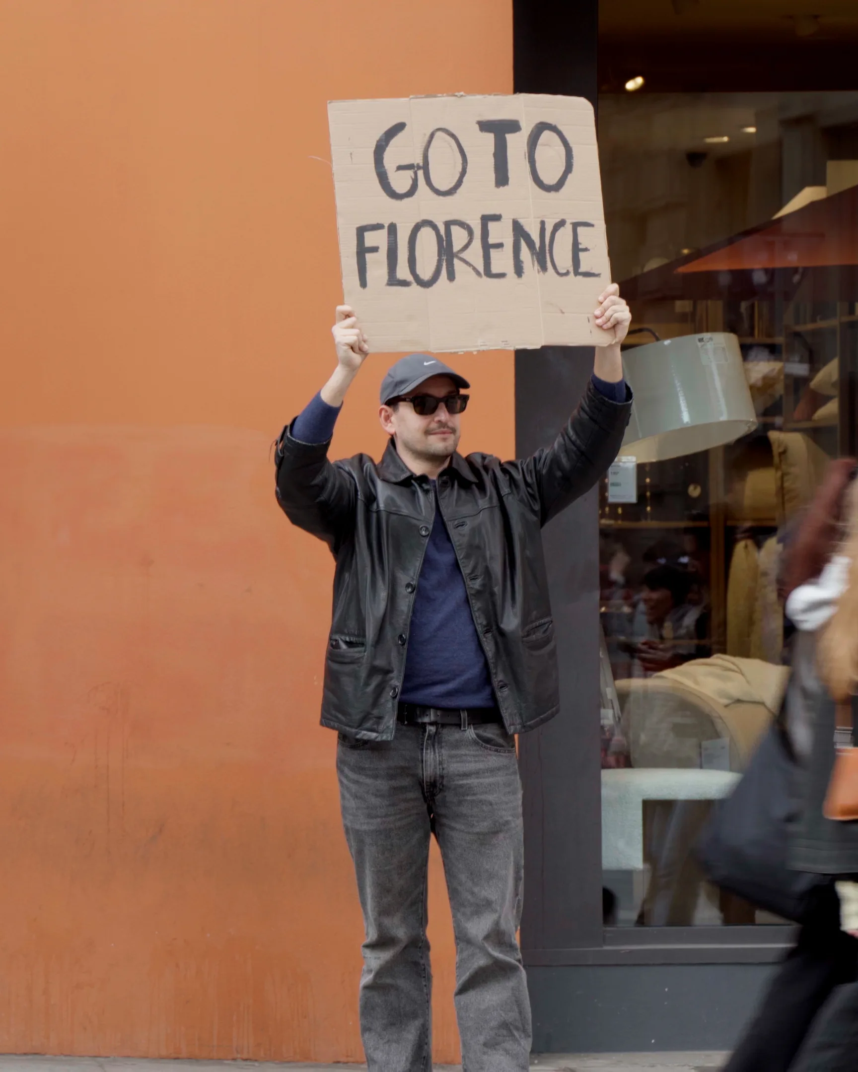 Cartello cartone: GO TO FLORENCE, contro un muro arancione